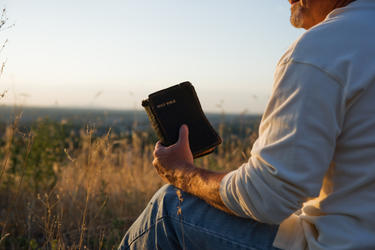 A man sitting on the ground holding an old Bible.