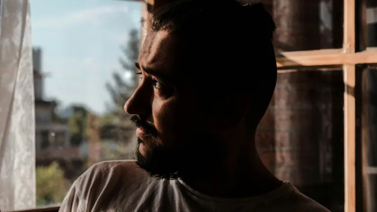 Yield your mind to God and good. a concerned man looking out through a window, his face in shadow
