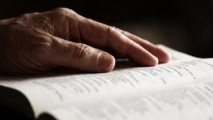 An older person's hand on a Bible.