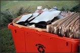 Recycling box filled with newspapers and crushed cans.