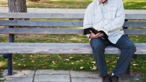 A man reading a Bible sitting on a park bench.