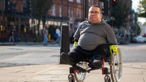 A man in a wheelchair going down a city street sidewalk.