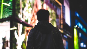 A man walking in a big city with lit billboards.