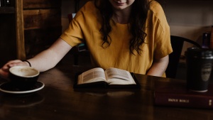 a woman sitting at a table with an open Bible and a coffee mug