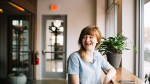 a woman indoors smiles as she sits up to a wooden table