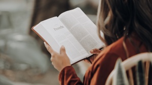 a woman sitting in a chair and reading a Bible, opened to the book of Proverbs