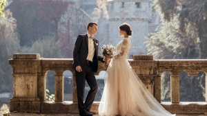 a groom and bride standing against a balcony with historic buildings in the background