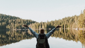 a woman with her arms raised in a joyful gesture facing a lake surrounded by trees