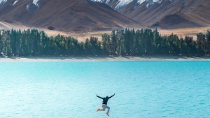 a person jumping in midair above a lake against a mountain backdrop