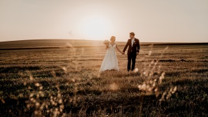 a bride and groom walking in an empty field at sunset