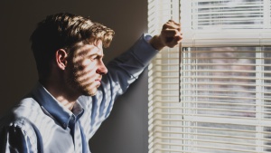 a man lifting a slat on the set of blinds on a window to look outside