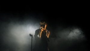 A man singing into a microphone on dark foggy stage.