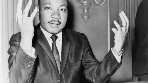 Rev. Martin Luther King, head-and-shoulders portrait, seated, facing front, hands extended upward, during a press conference.