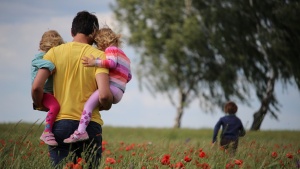 A father walking in field carrying two daughters.