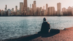 A person sitting near the edge of water looking at a city skyline.