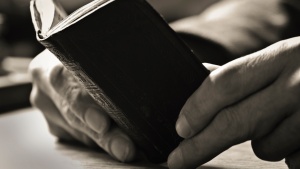 A man's old hands holding a small Bible.