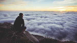 A man sitting on a rock looking out over the clouds covering a valley.