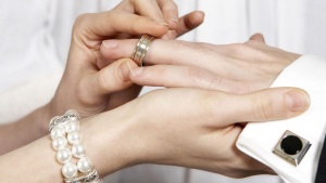 A woman putting a wedding ring on her husband.