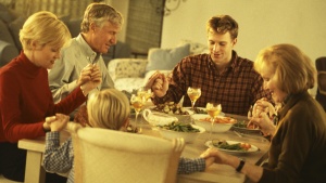 A family holding and praying before eating a meal.