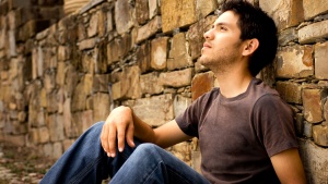 A young man sitting against a rock wall.