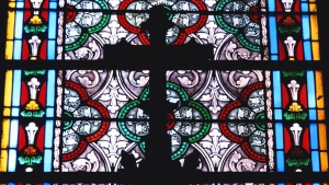 A cross and stained glass window inside a large church.
