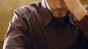 A man with his hand holding his head while looking down at a Bible.