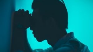 A man with his head and hand resting against a wall.