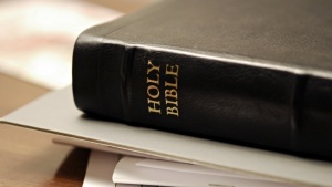 A Bible stacked on top of papers laying on a table.