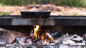 A cast iron skillet on a fire grate with hot flames underneath.