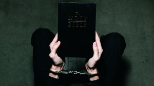 A person holding a Bible while their hands are wearing shackles.