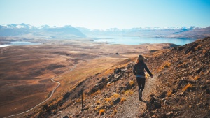 A woman running on a rugged trail on a mountain side.