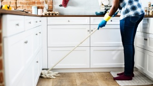 A person cleaning a kitchen floor with a mop.