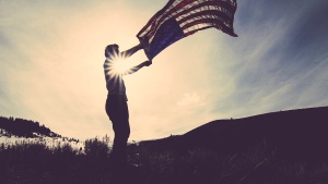 A man holding an American flag flapping in the wind.