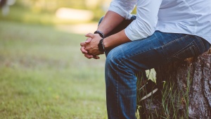 A man sitting on a stump with his hands clasped. 