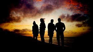 A silhouette of four people at dusk near a body of water.