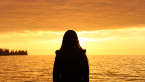 Woman standing by a body of water when the sun is setting.