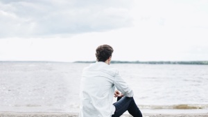 A young man sitting on the shore a lake - looking at the water.