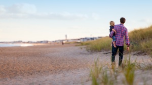 A father carrying his small child on the beach.