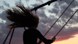 A woman swinging on a playground swing at sunset.