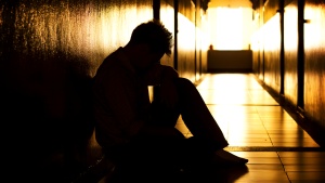 A person sitting with the head down in a dark hallway.