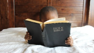 A little lying in bed looking at a Bible.