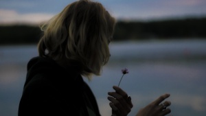 A woman holding a wilting flower in her hand.