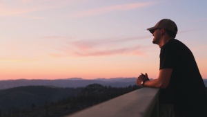 A young man watching the sun set from an observation deck.