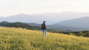 A man hiking in field with mountains in the background.