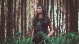 A young woman staring up while standing in tall grass near trees.