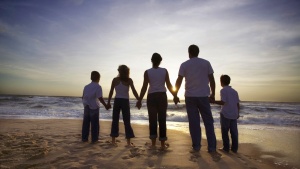 A family holding hands looking at the ocean waves and the sun setting.