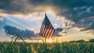 A small United States flag in the grass with the sun setting in the horizon.