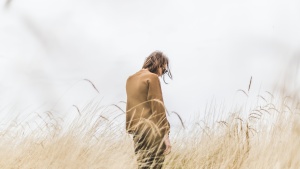 A woman standing in tall grass looking down.