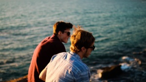 Two young men talking to each other by the ocean.