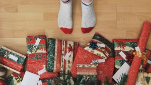 A person with socks standing right beside Christmas gifts. 